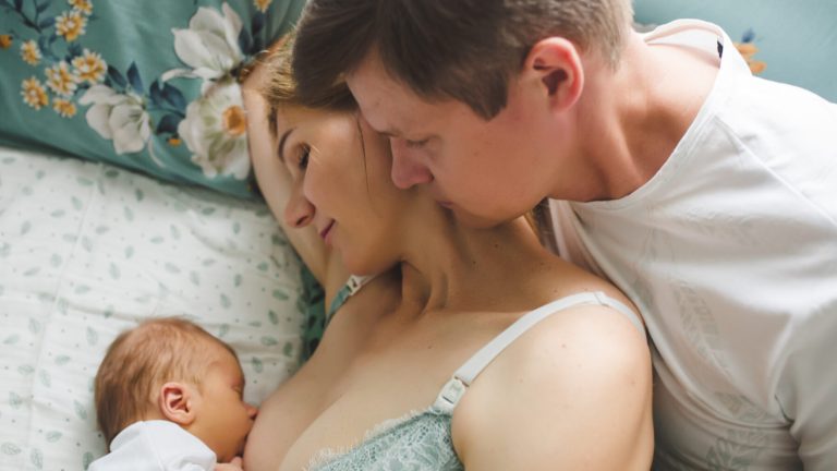 Young mother breastfeeding her newborn baby son. Happy father looking at them. Breast feeding and lactation infant.