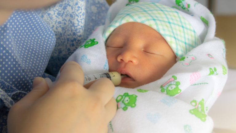 Mother feeding newborn baby milk with syringe