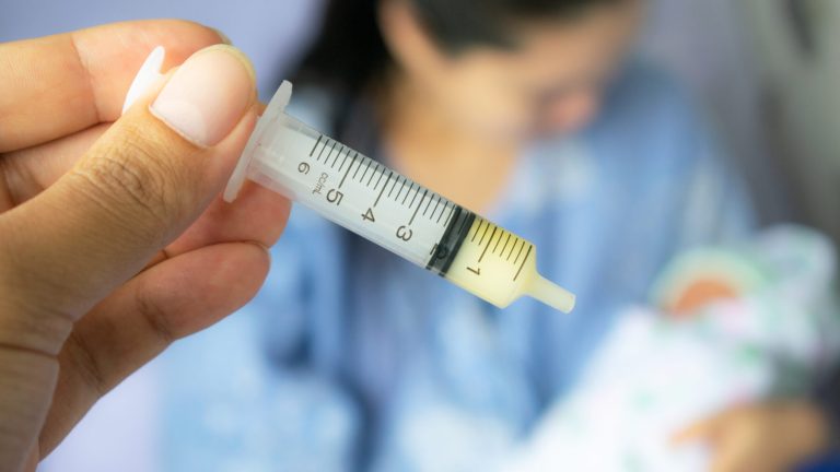 Mother feeding newborn baby milk with syringe