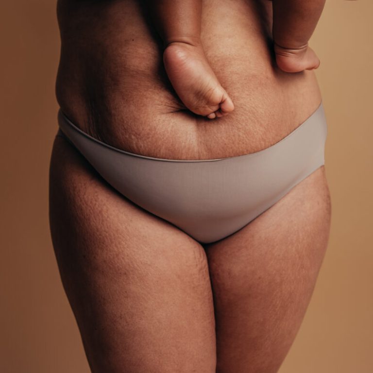 Cropped shot of a healthy female carrying her baby. Close-up of a woman in underwear with feet of child on postnatal belly.