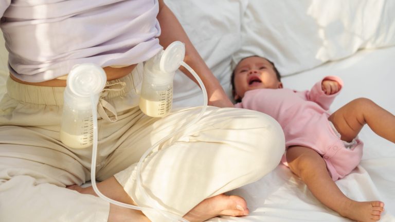 mother using breast pump machine to pumping milk with her newborn baby on a bed