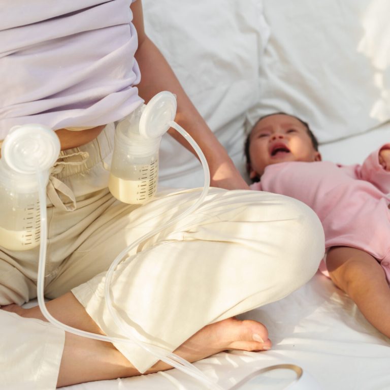 mother using breast pump machine to pumping milk with her newborn baby on a bed
